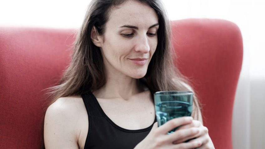 A relaxed woman in black top holding a glass of water and smiling, sitting indoors.