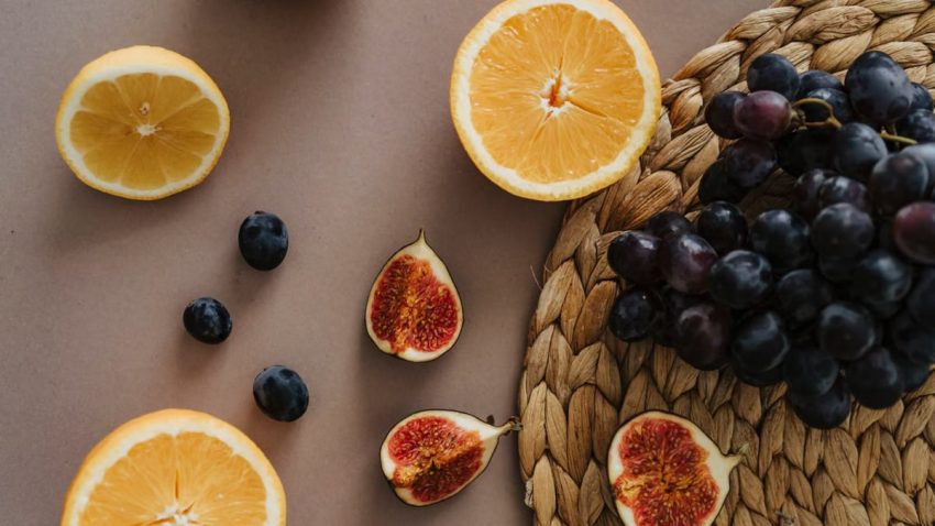 High-angle view of sliced citrus, figs, and grapes on a woven mat, showcasing fresh produce.